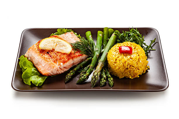 Garnished fried salmon steak with boiled green asparagus and rice with turmeric on white background