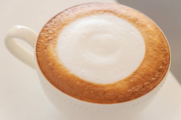 Creamy cappuccino with frothy milk foam and golden crema in white ceramic cup, warm inviting breakfast beverage
