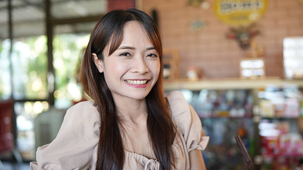 Young woman with long hair smiles warmly in cozy cafe setting, showcasing friendly and inviting atmosphere