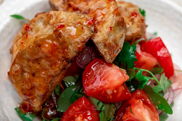 A close-up shot of homemade golden-brown fried eggplant pieces served on a bed of fresh mixed greens, cherry tomatoes, and red onions. The dish is presented on a textured ceramic plate set on a natural grey linen tablecloth. This rustic, healthy appetizer is perfect for a family dinner or a restaurant menu illustration.