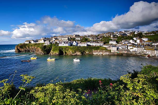 Port Isaak coastal village and harbour in Cornwall, BG. Summer sunshine, blue sky, some clouds, small boats, calm water, idyllic scene with some green in front.