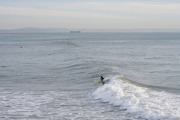 Estoril Portugal December 17 2025. A surfer rides a small ocean wave near the shoreline under calm winter conditions.