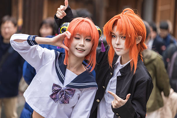 Kyoto, Japan - December 06, 2025: Two enthusiastic cosplayers with vibrant orange wigs and anime-inspired makeup pose playfully outdoors. One wears a sailor uniform, the other a black jacket,