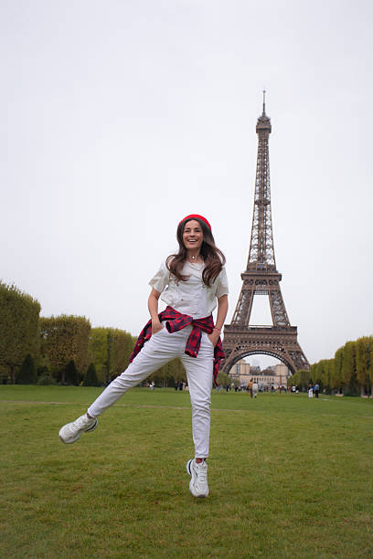 Woman with blond hair, wearing a white hat and white jacket holding hands with her boyfriend while running on a bridge at seine river to see Eiffel Tower Paris, rear view, cloudy day, horizontal