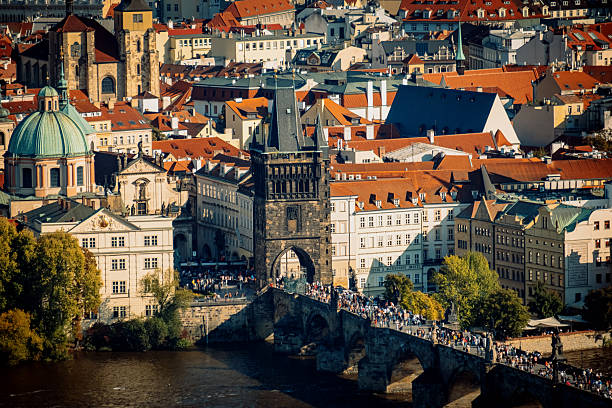 Historic Charles Bridge Tower With Pedestrians And Statues, Lively Midday Crowd And Musician Performing