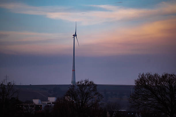 Single wind turbine standing on a distant hill under a pastel evening sky. Renewable energy concept with clean power generation, sustainability, and modern energy transition in a rural environment.