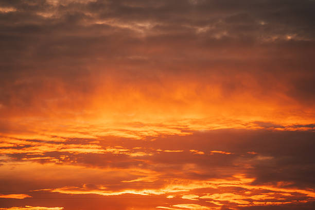 Close-up view of an intense sunset sky filled with glowing orange and red clouds. The dramatic natural light and cloud formations create an abstract atmospheric background suitable for themes of nature, weather, and climate.