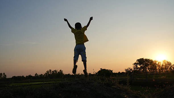 Child joyfully jumps on mound during sunset, silhouetted against vibrant sky. scene captures sense of freedom and happiness