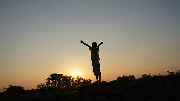 A boy jumps with joy in an open natural field near a lake, representing childhood energy, fun, and freedom in the wild outdoors.