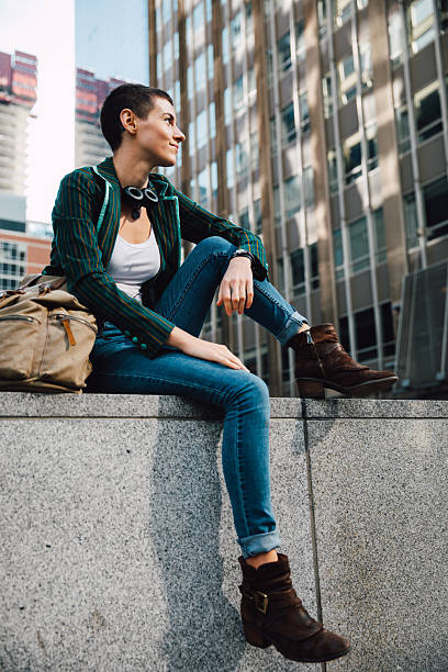 Casual portrait of a woman seated outdoors in an urban environment, with modern buildings in the background.