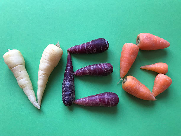 White, Purple and orange carrots spelling the word veg, isolated o green background