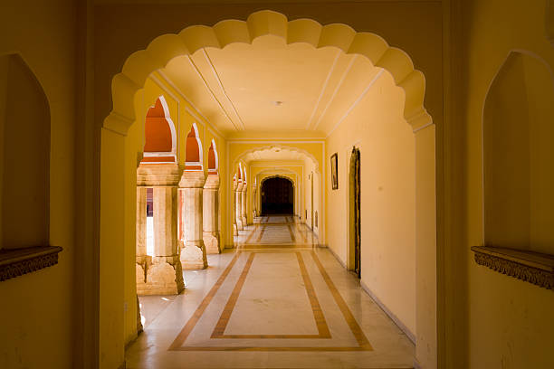 Jaipur, India - March 16, 2022: An arched corridor inside City Palace at Pritam Chowk is shown with yellow painted walls, marble flooring, decorative columns, and natural light illuminating the passageway.