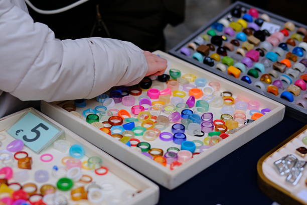Hands of people browsing and exchanging rings at a second-hand market stall. A variety of vintage and costume jewelry is displayed on a table, capturing everyday interactions, local commerce, and the atmosphere of a used goods market. No faces visible.
