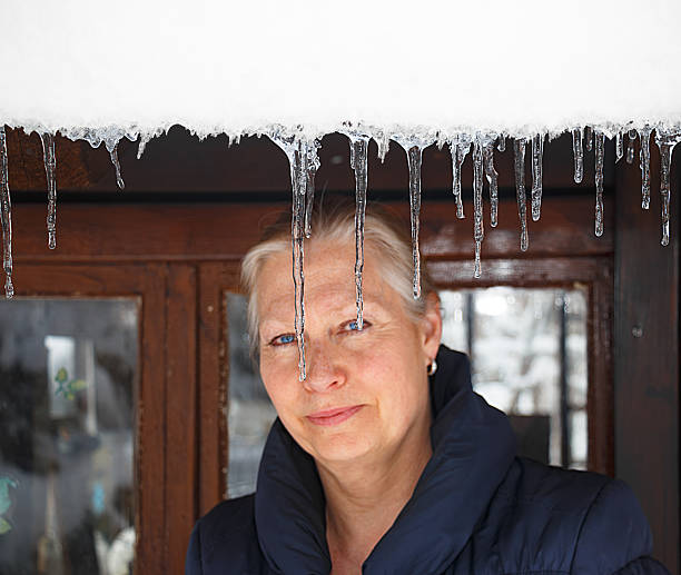Portrait of a beautiful blonde woman in front of her house, snow and icicles hanging from the roof.