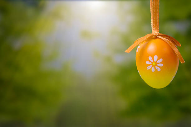 Easter egg hanging background yellow orange gradient floral pattern blurred green nature park scenery with copy space for banner design concept of holiday, decoration, celebration.