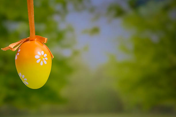 Easter egg hanging background yellow orange gradient floral pattern blurred green nature park scenery with copy space for banner design concept of holiday, decoration, celebration.