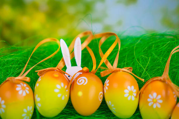 easter bunny background orange yellow floral pattern white rabbit ears peeking from grass behind row of eggs with copy space for banner design concept of holiday, surprise, celebration.