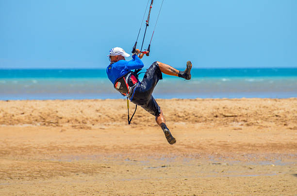 Hurghada, Egypt - July 16, 2015: A young man is standing in a motorboat parked on the sandy shore. He is piloting a kite in the air with one hand and holding a kiteboard with the other, preparing for a session.