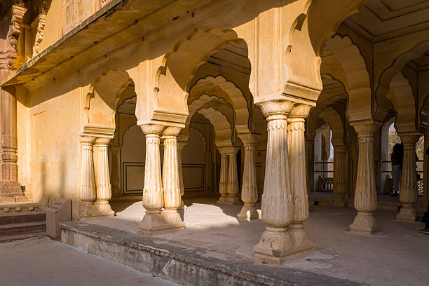 Amber, India - March 16, 2022: The image shows a close view of carved stone columns and arches at the Diwan-e-aam pavilion in Fort d'Amber, with sunlight and shadows on the yellow stone surfaces.