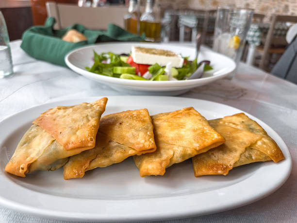 Traditional Greek spinach pies served on a white plate in a seaside tavern. Crispy filo pastry filled with spinach and herbs, typical Mediterranean appetizer in Greece.