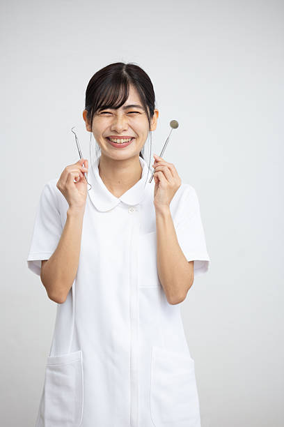 Smiling Woman in White Uniform Holding Dental Instruments on White Background