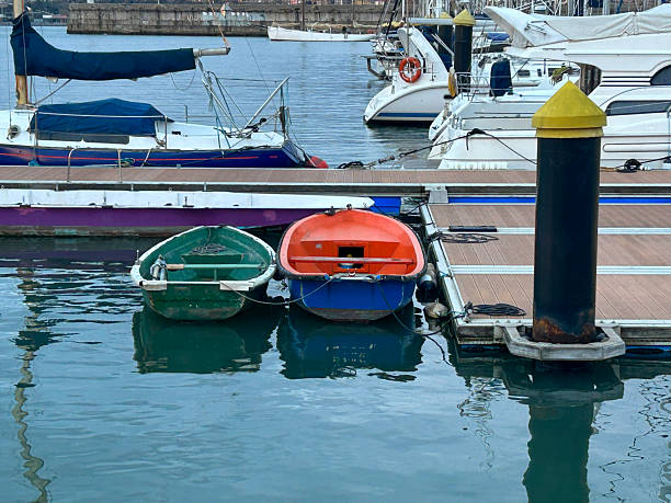 Two small rowboats floating calmly beside a wooden dock with yachts in the background