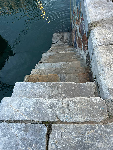 Rough stone steps leading down into dark water with light reflections