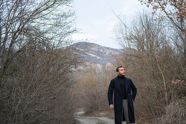 Man wearing an overcoat and turtleneck standing on a path in a bare winter forest