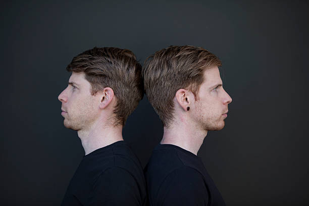 Studio-style profile portrait of identical twin brothers standing back to back against a dark neutral background. Clean composition and mirrored poses emphasize symmetry, identity, and comparison. Commercial image with model release.