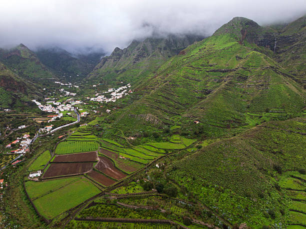 Clouds over rugged green mountains with terraced fields and a small white village nestled in the valley, Agaete municipality, Gran Canaria, Canary Islands, Atlantic Ocean, Spain