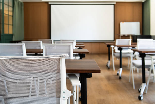 Empty lecture hall with rows of seats, desk and projection screen