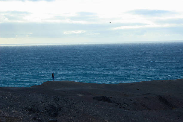 Rear view of a man standing and admiring the vast Atlantic Ocean during a beautiful sunset. Silhouette scene with warm colors, calm sea, and emotional atmosphere representing freedom, reflection, travel, and inspiration.