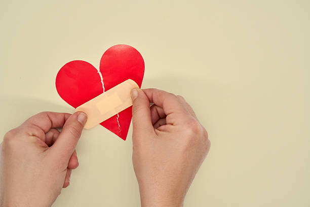 Hand Applying Band Aid To Broken Red Heart Shaped Torned Paper