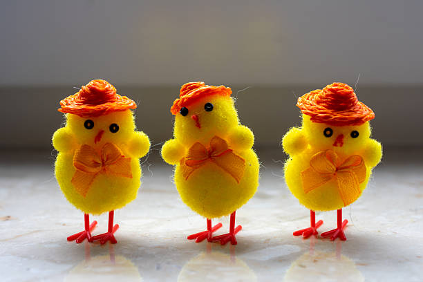 Three yellow chicks with orange hats and bows. One is standing in front of the other two. The hat is orange and the bow is yellow.
