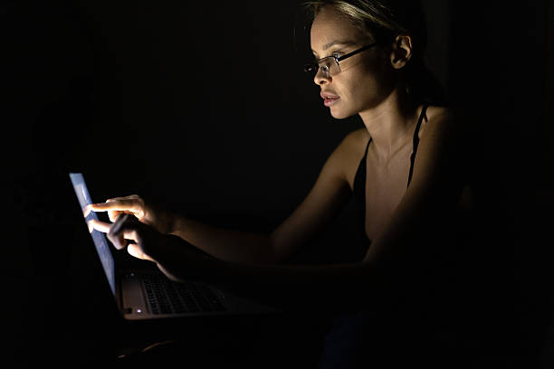 Beautiful woman, freelancer, working from home at night. Sitting at the desk in her living room and working on laptop in dark room