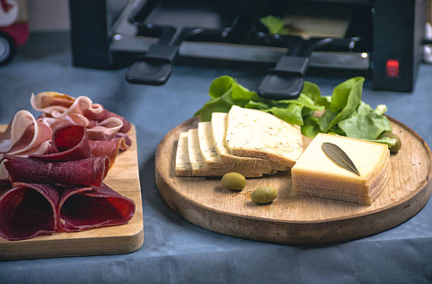 An inviting raclette spread featuring melted cheese, salami, ham, and vegetables. A perfect combination of traditional flavors and Christmas, new year
