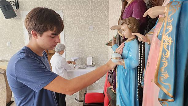 A young boy practicing his faith, while in the background the minister is preparing for the celebration.