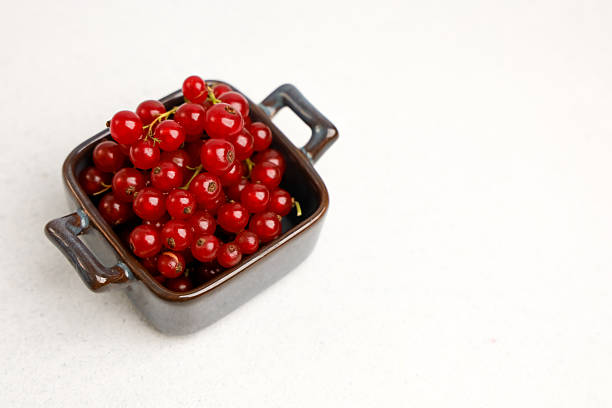 A bowl with red berries sits on a light surface in a kitchen. The bowl has two handles and the berries are fresh and round. This scene shows simple food preparation in a home.