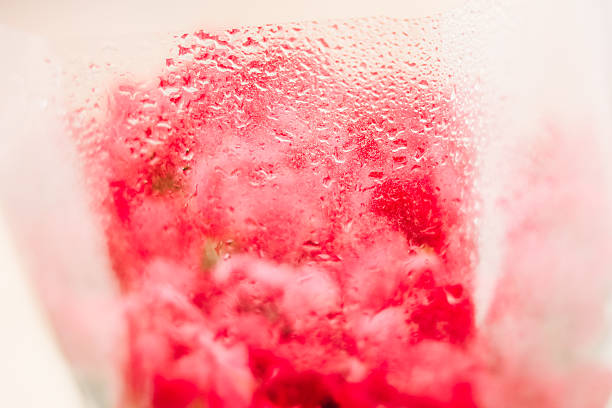 A clear glass shows water droplets forming on its surface. Inside there are red items creating a striking contrast. The background is slightly blurred enhancing the focus on the glass.