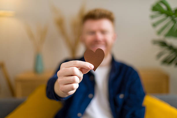 Male person holding a brown paper heart cutout, showing affection and kindness for valentine's day or charity concept
