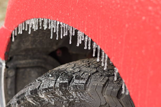 Car's undercarriage covered in hanging icicles, parked in fresh white snow during winter creating dangerous driving conditions with freezing cold weather and ice on the ground
