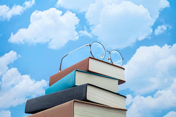 istock Stack of books with eyeglasses against a blue sky with clouds. 2258187777