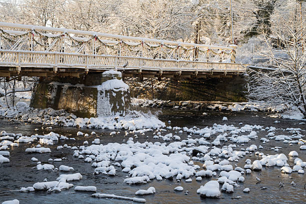 Winter landscape. A small wooden bridge of white color is spanned over a small ravine covered with snow.
