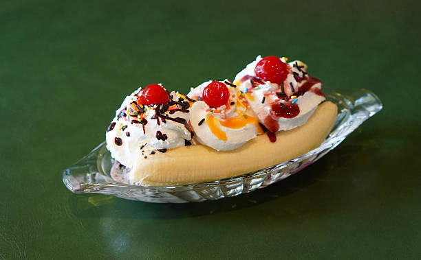 cool ice cream, decorated with whipped cream and cherries and top with orange jam, strawberry jam, chocolate jam and slice banana split, served in a boat-shaped glass on green leather floor background, dessert, food, ice, copy space