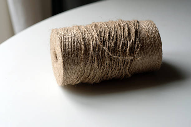 A spool of brown twine rests on a smooth white table. Bright light shines in from a window. The setting looks simple and captures the texture of the twine.