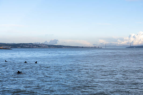 Oeiras Portugal November 21 2025. Surfers wearing wetsuits float on surfboards in calm Atlantic waters with distant shoreline visible.