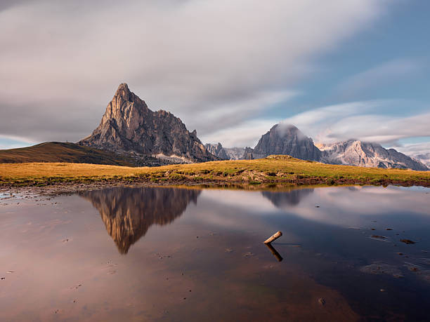 Majestic mountain peaks reflected in a calm lake at Pasa Giau under a soft, cloudy sky. Photographed in medium format.