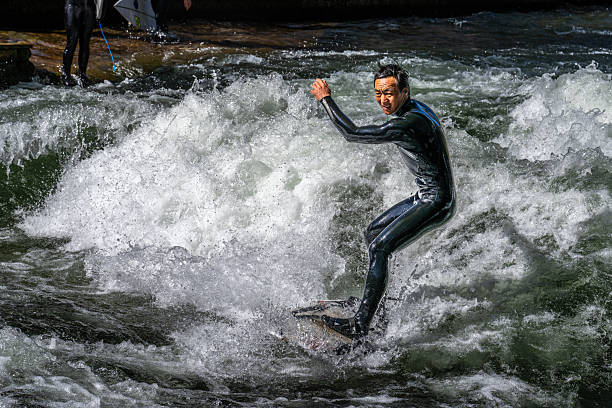 Munich, Germany - Apr 12, 2025: Surfer in the city river, Munich is famous for people surfing in urban enviroment called Eisbach. Surfers practicing their skill on an artificial wave in central Munich