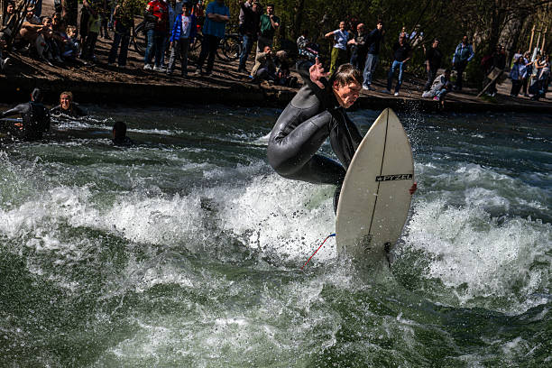 surfer riding the wave of the Eisbach river in the English Garden,Winter surfing in an urban environment, an extreme sport on icy water surrounded by a natural park, Munich, Germany 21 February 2025