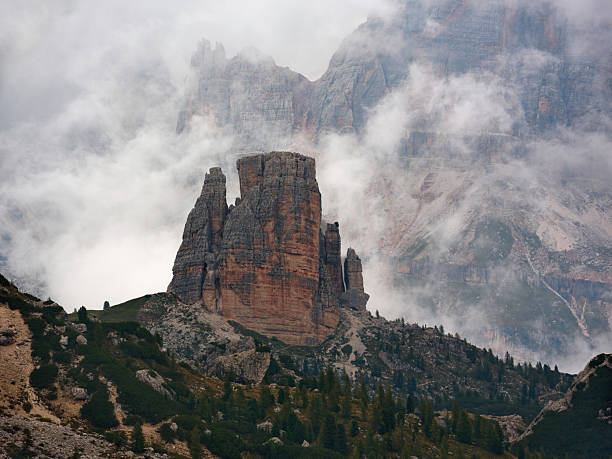 Impressive Cinque Torri rocky mountain rising through low clouds and fog, creating a moody and dramatic alpine scene. Photographed in medium format.